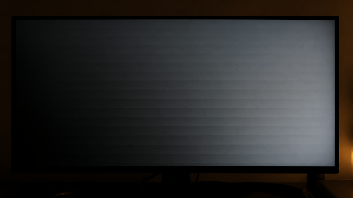 A widescreen monitor in a dim room showing a dark near-black grey ramp with obvious horizontal banding stripes in the shadows.