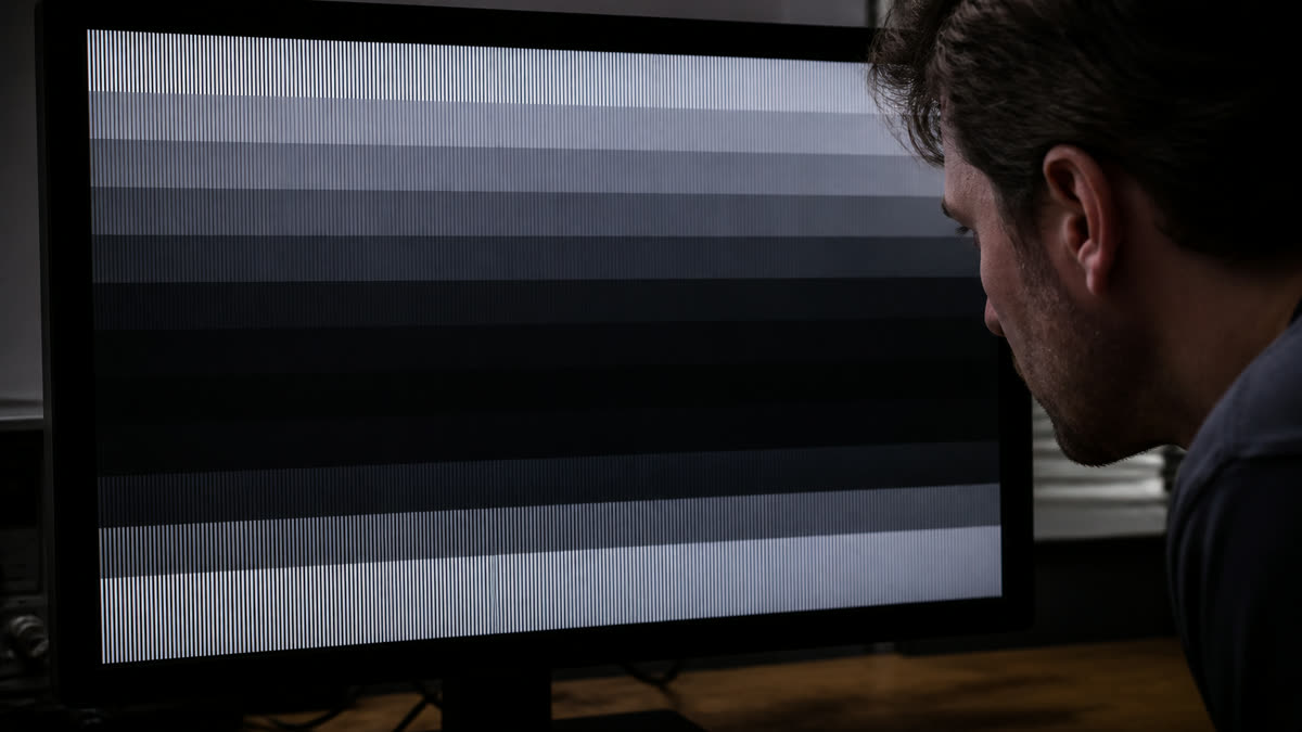 A monitor gamma test where midtone bands look crushed and too dark while someone inspects the panel.