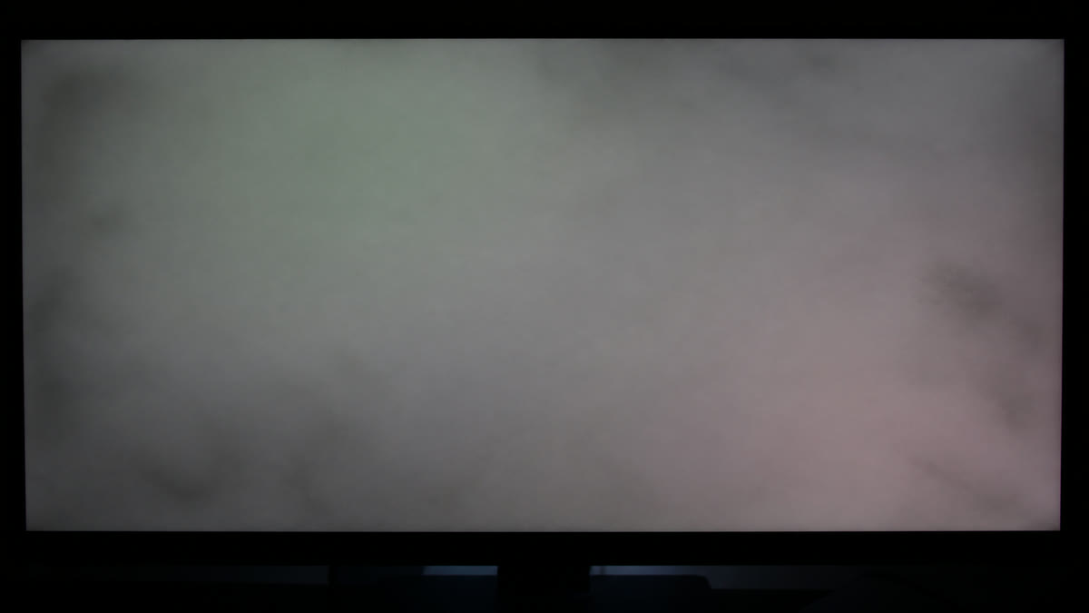 A monitor showing a solid mid-gray field with blotchy dirty-screen clouds and a faint green-pink tint from center to corner.